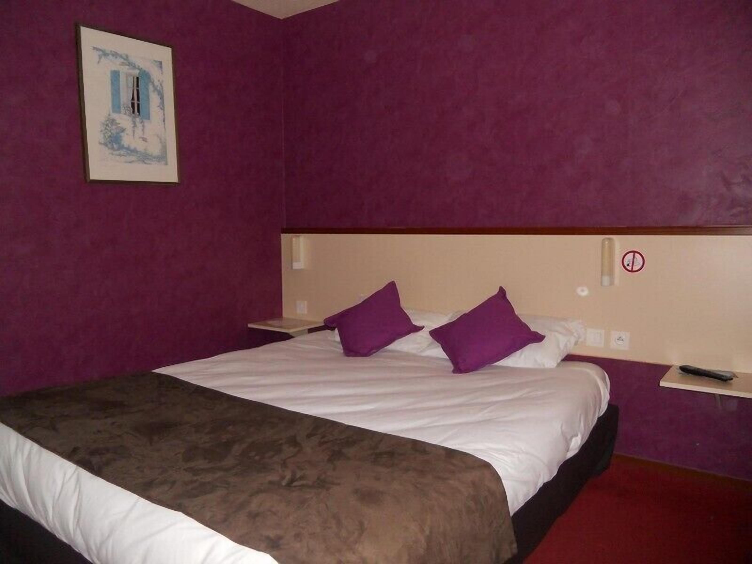A hotel room with a large bed, purple pillows, a headboard, and a painting on the wall.