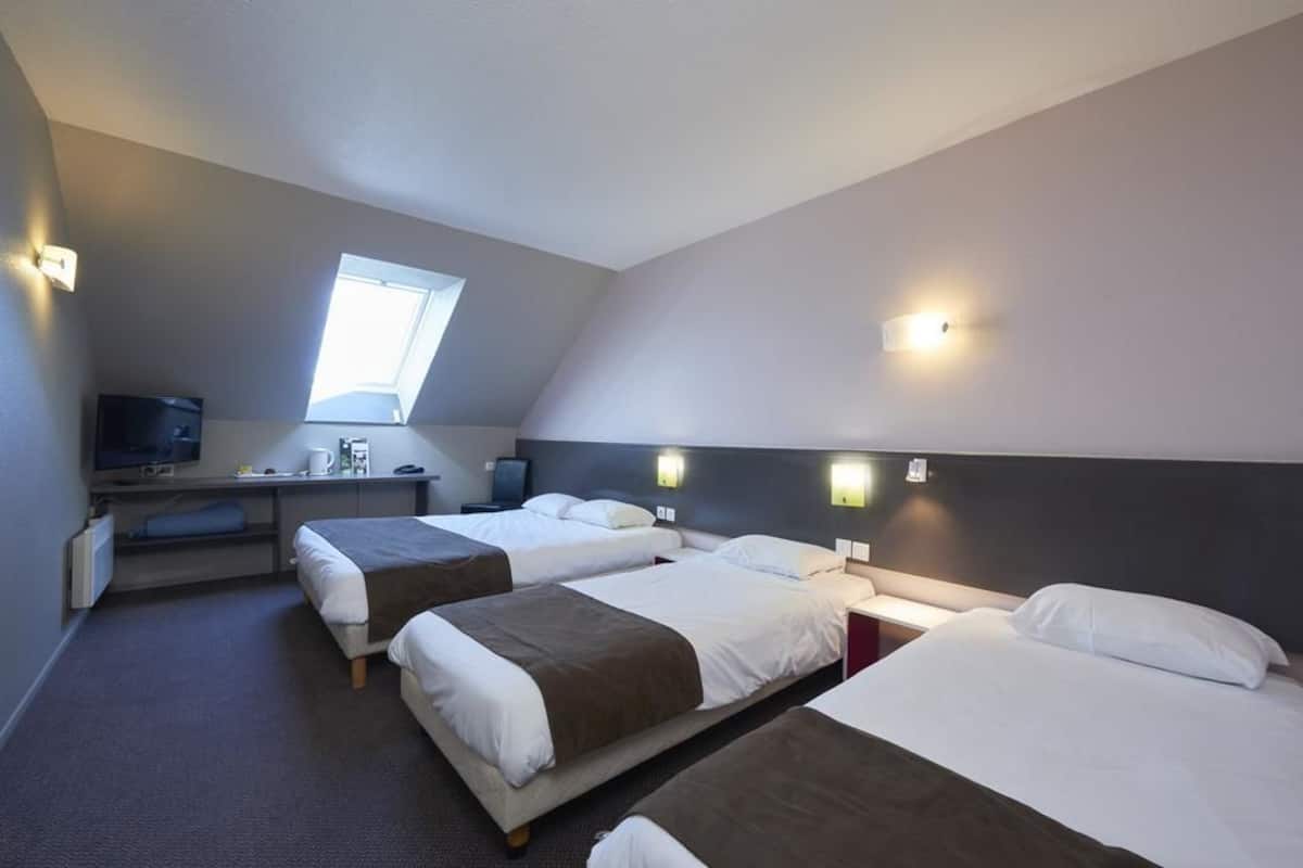 Habitación de hotel con tres camas, un escritorio con computadora, televisión y tragaluz.
