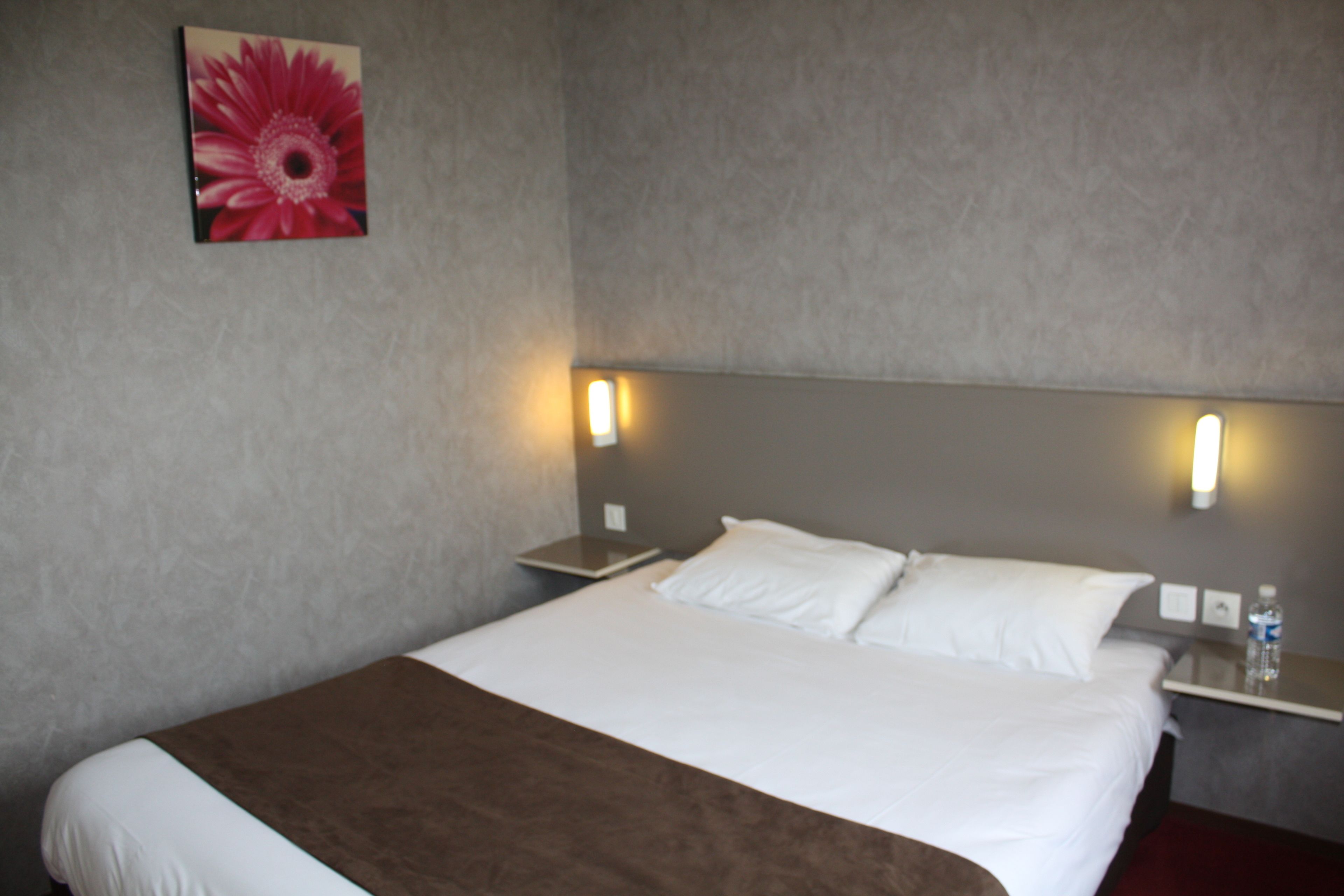 Una habitación de hotel con una cama grande, dos mesitas de noche, una lámpara de pared y un cuadro de una flor.