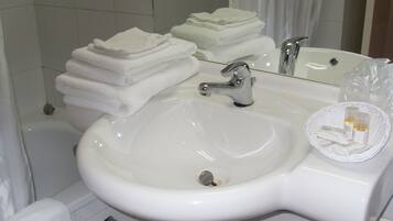Un lavabo blanc dans une salle de bain, avec un miroir au-dessus, une pile de serviettes blanches et un panier en osier contenant des articles de toilette.
