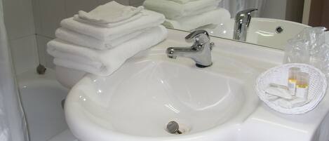 A white bathroom sink with a mirror above it, a stack of white towels, and a wicker basket with toiletries.