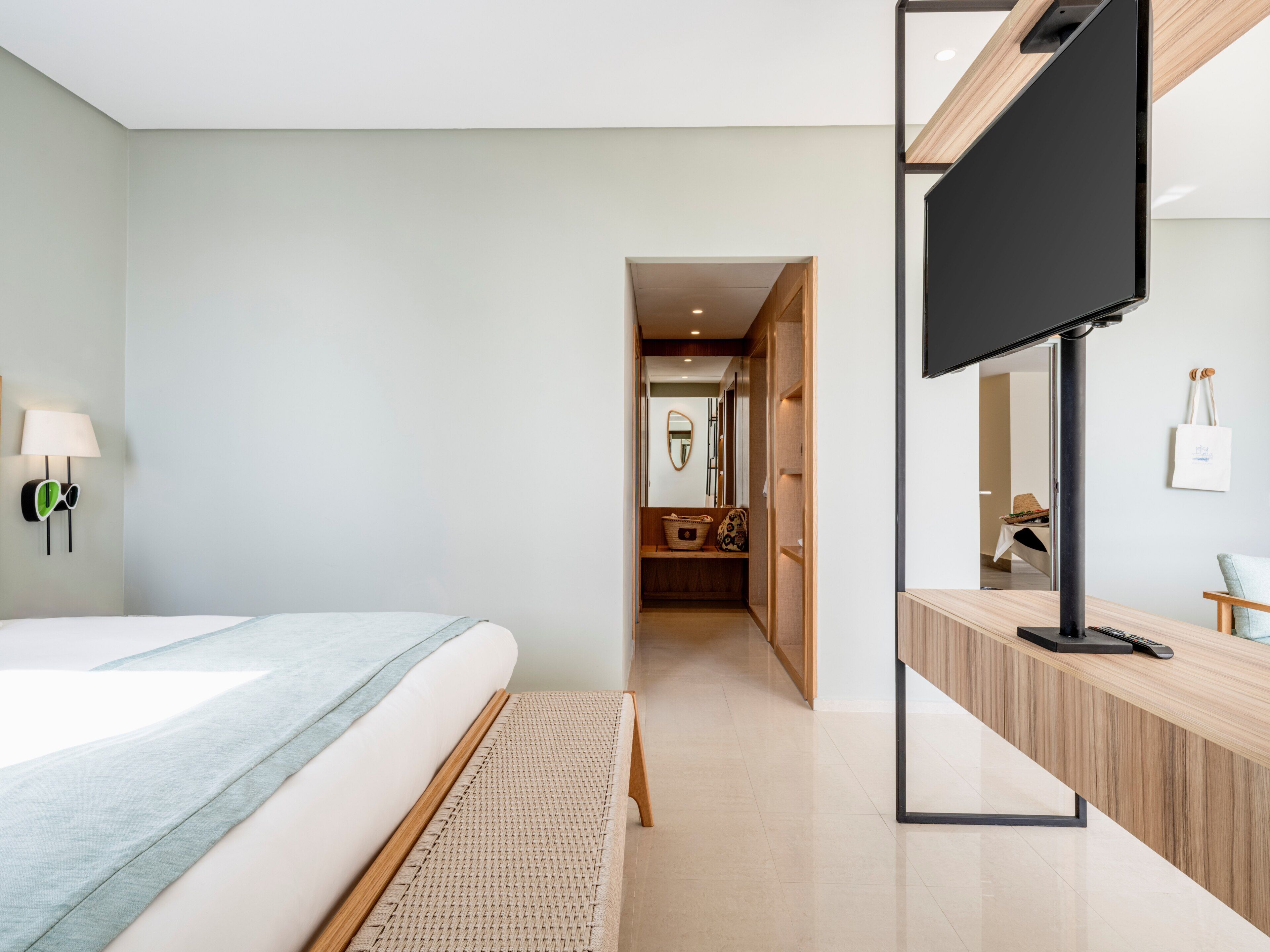 A modern hotel room with a bed, a flat-screen TV, a wooden desk, and a mirror.