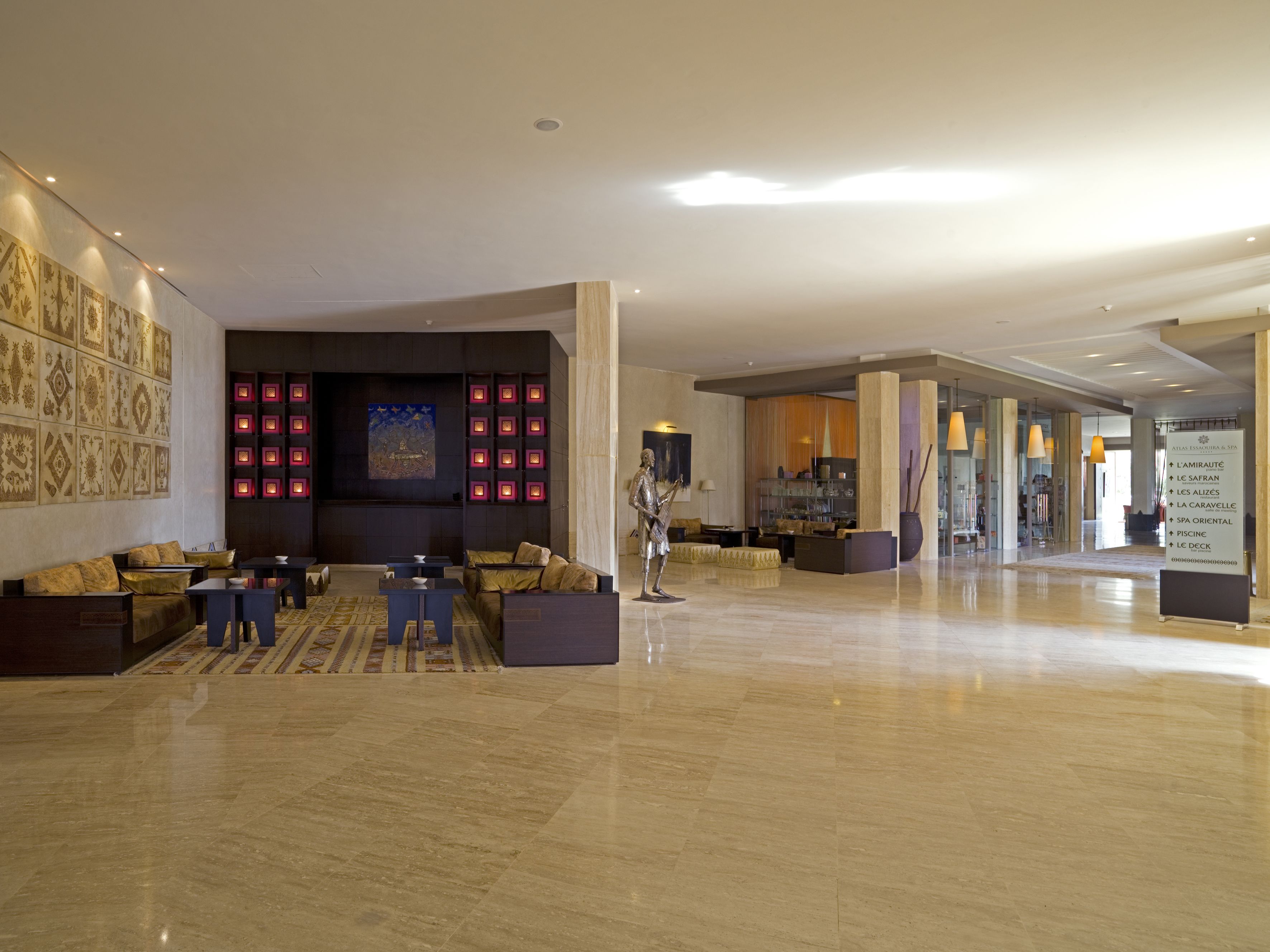 Un hall d’entrée spacieux avec un coin salon, un grand mur orné de carreaux décoratifs et un panneau indiquant les équipements disponibles.