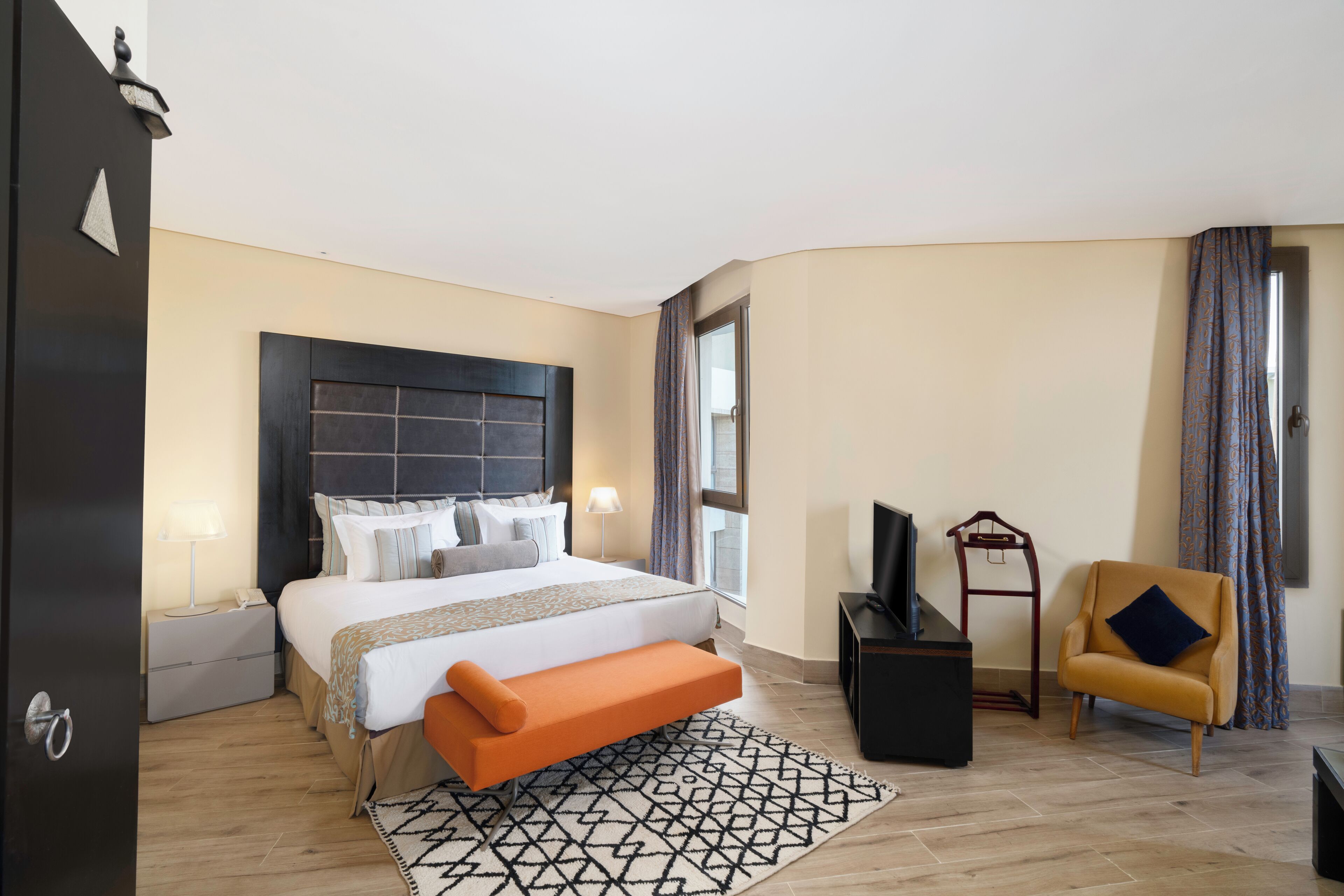 A hotel room with a large bed, a bench, a TV, a chair, and a desk.