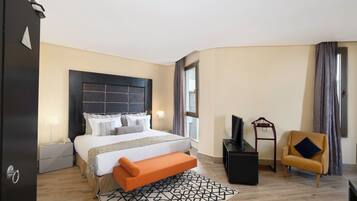 A hotel room with a large bed, a bench, a TV, a chair, and a desk.