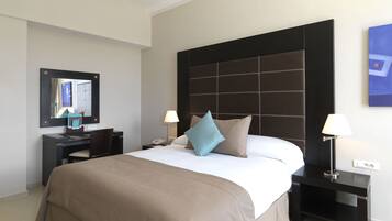 Une chambre d’hôtel avec un grand lit, un bureau, une chaise, une table de chevet, une lampe, un miroir et un tableau au mur.
