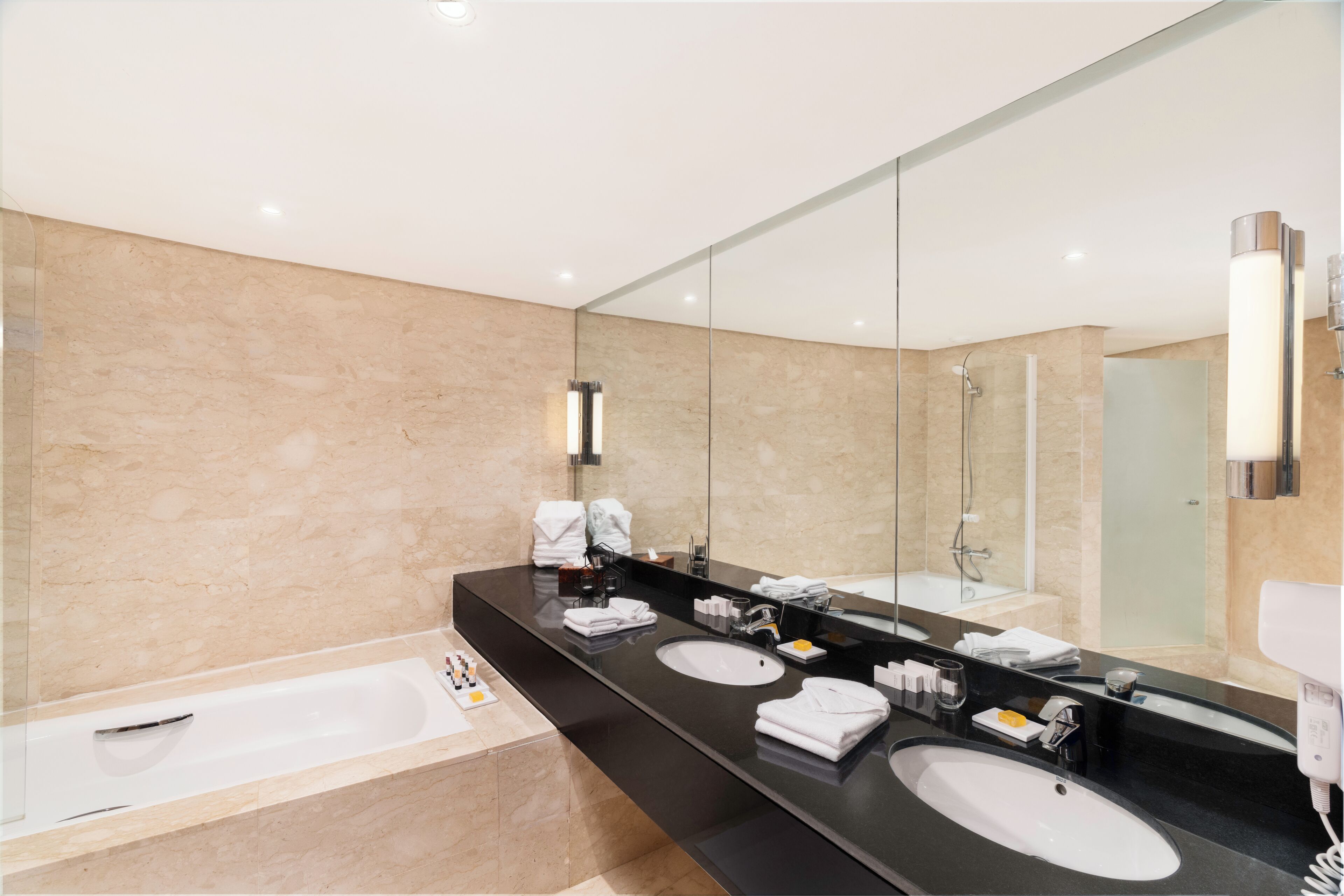 Une salle de bain moderne avec un grand miroir, deux lavabos, une baignoire et une douche.