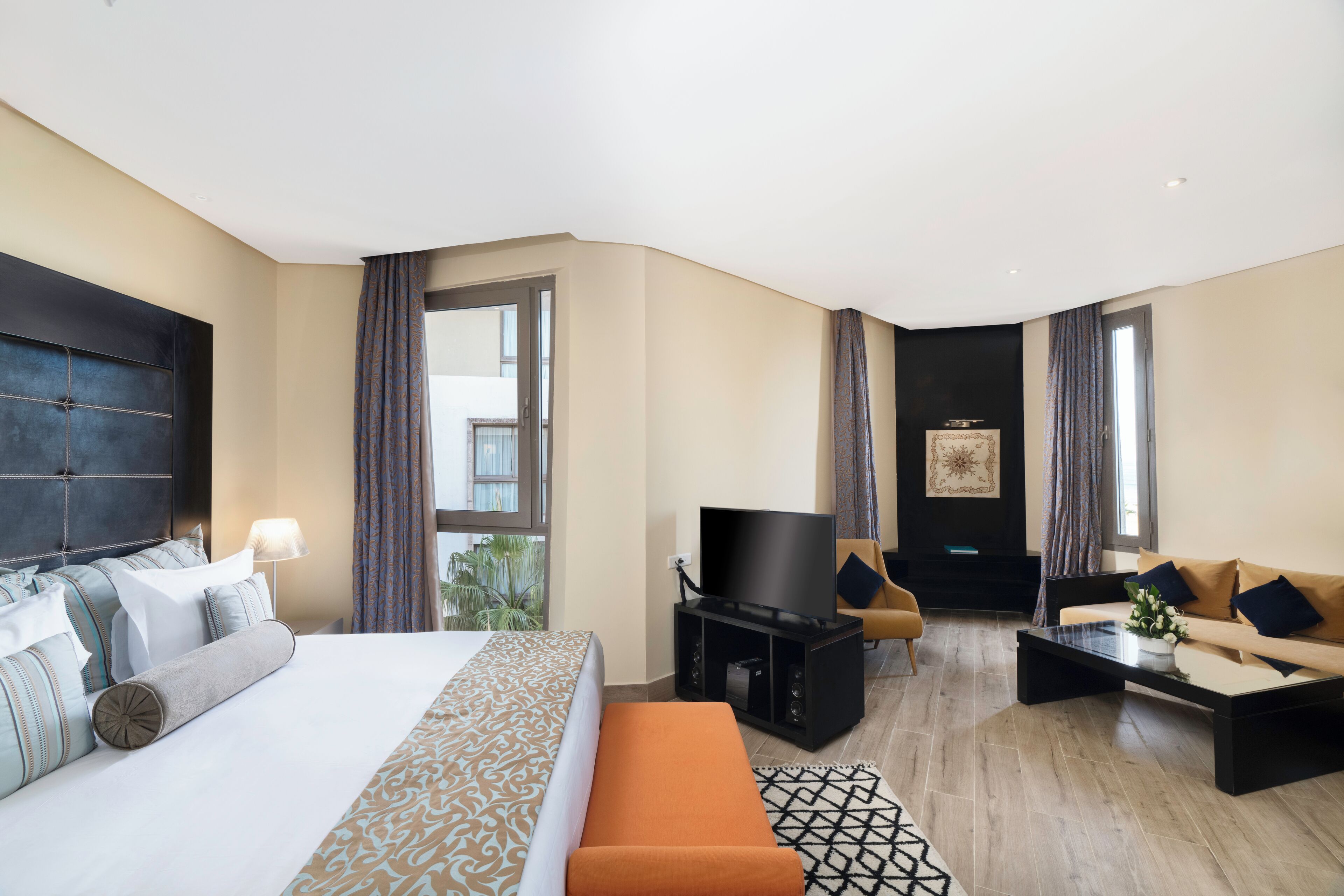 A hotel room with a large bed, a sofa, a coffee table, and a TV.