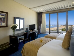 A hotel room with a desk, TV, and large windows offering a beach view. - Atlas Essaouira Riad Resort (Essaouira)