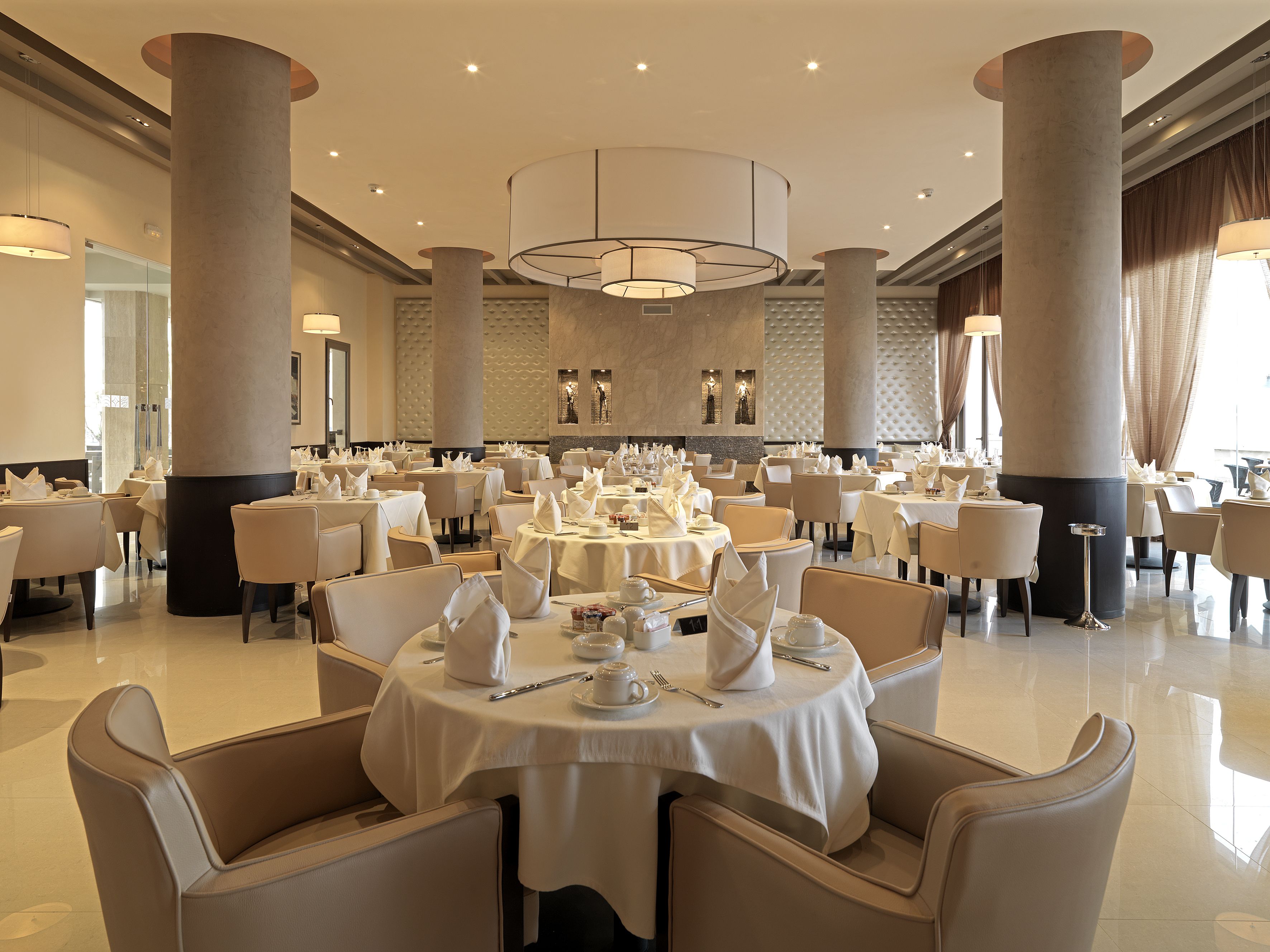 A spacious dining area with round tables, high-backed chairs, and large columns.