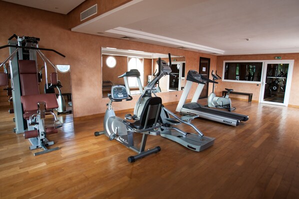A gym with various exercise machines, a mirrored wall, and a wooden floor. - Tikida Golf Palace (Inezgane)