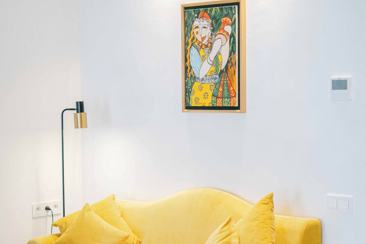 A yellow sofa with matching cushions, a black floor lamp, and a framed artwork on the wall.