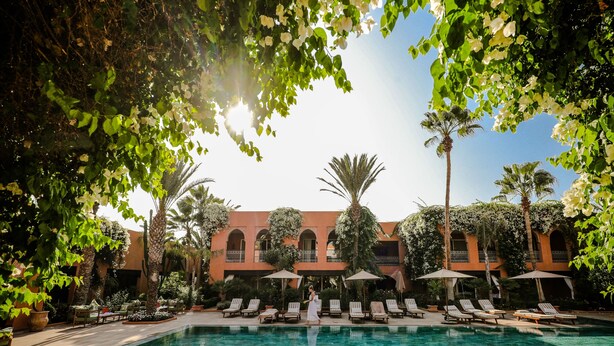 A pool area with lounge chairs, umbrellas, and a building with arched windows and balconies. - Tikida Golf Palace (Inezgane)