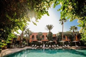 A pool area with lounge chairs, umbrellas, and a building with arched windows and balconies. - Tikida Golf Palace (Inezgane)