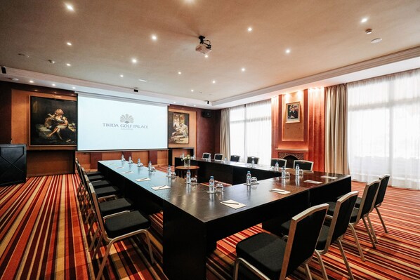 A conference room with a long table, chairs, a projector screen, and a carpeted floor. - Tikida Golf Palace (Inezgane)