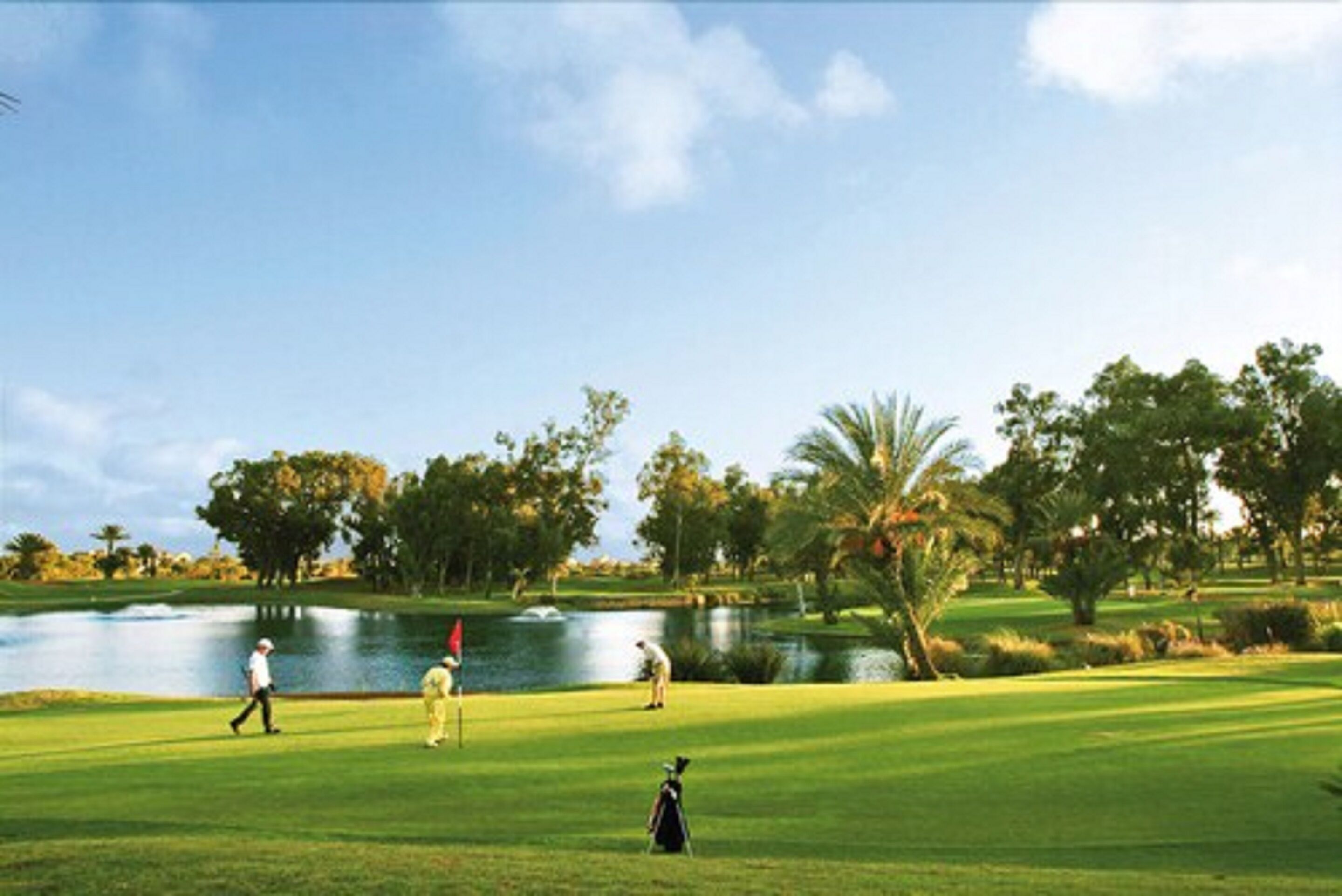 Un campo de golf con un estanque, árboles y cielo despejado.