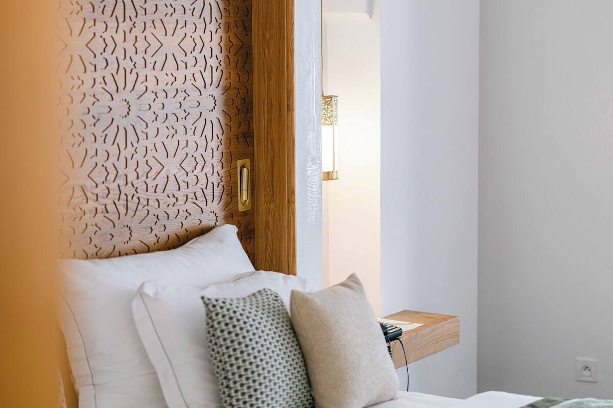 A bedroom with a bed, pillows, a nightstand, and a wall with a decorative panel.