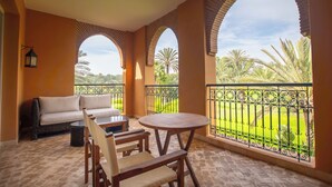 A balcony with a sofa, chairs, and a table, overlooking a well-maintained garden with palm trees. - Tikida Golf Palace (Inezgane)