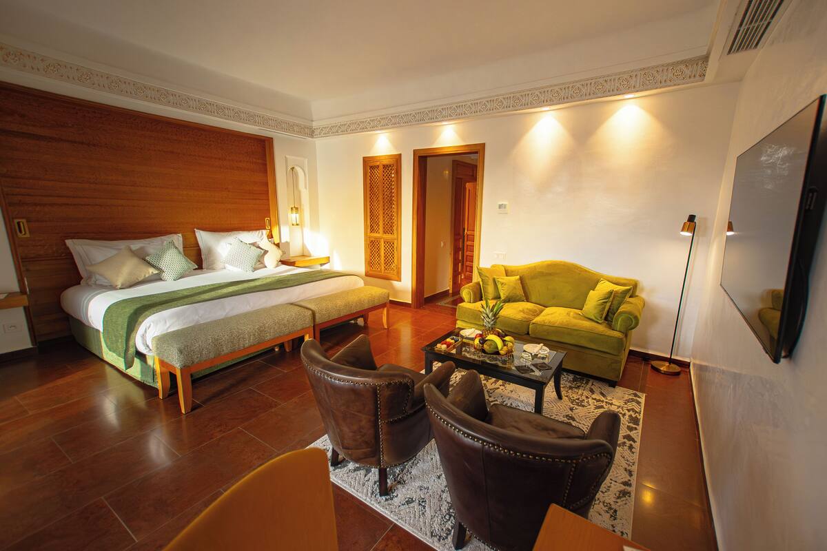 A hotel room with a bed, a sofa, two armchairs, a coffee table, and a television.