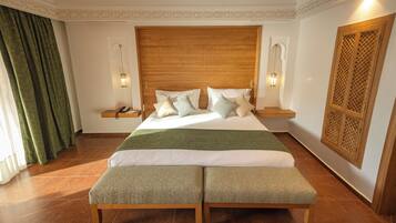 Un dormitorio con una cama grande, dos mesitas de noche, un banco, un cabecero decorativo y un panel de madera en la pared.