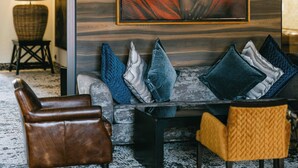 A modern living room with a large painting, a brown leather armchair, a yellow armchair, and a black sofa with patterned cushions. - Tikida Golf Palace (Inezgane)