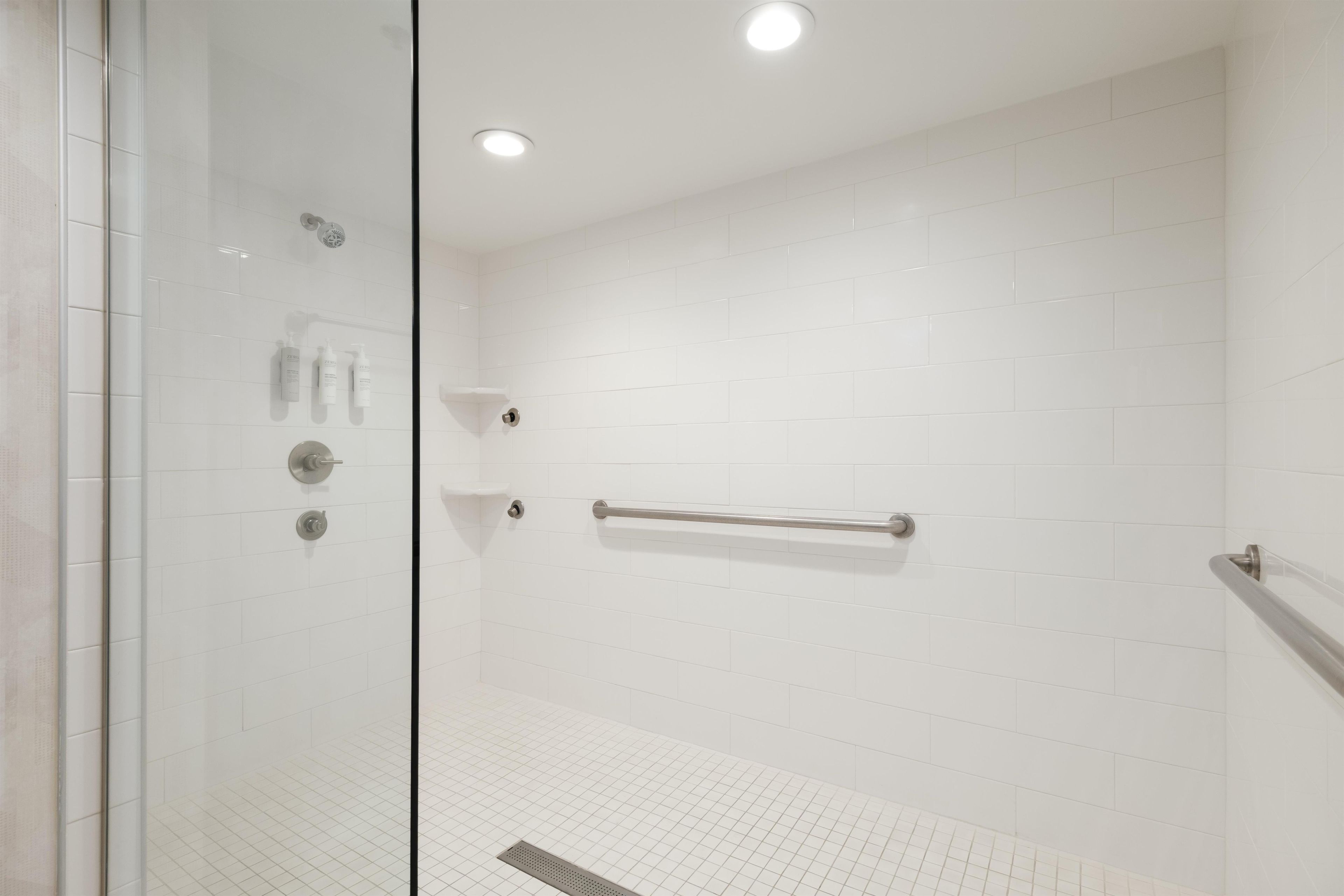 A glass-enclosed shower with white tiles, a handrail, and a control panel.