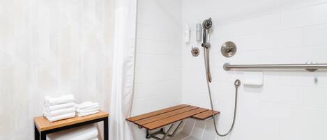 A shower area with a bench, a towel rack, and a showerhead.
