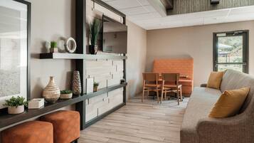 A modern living room with a sofa, ottomans, a TV, and a dining area with chairs and a table.