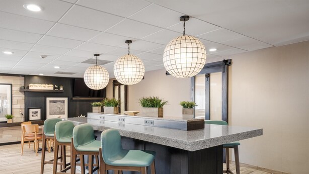 Una cocina moderna con una isla central, taburetes de bar, iluminación colgante y vistas al área de comedor.