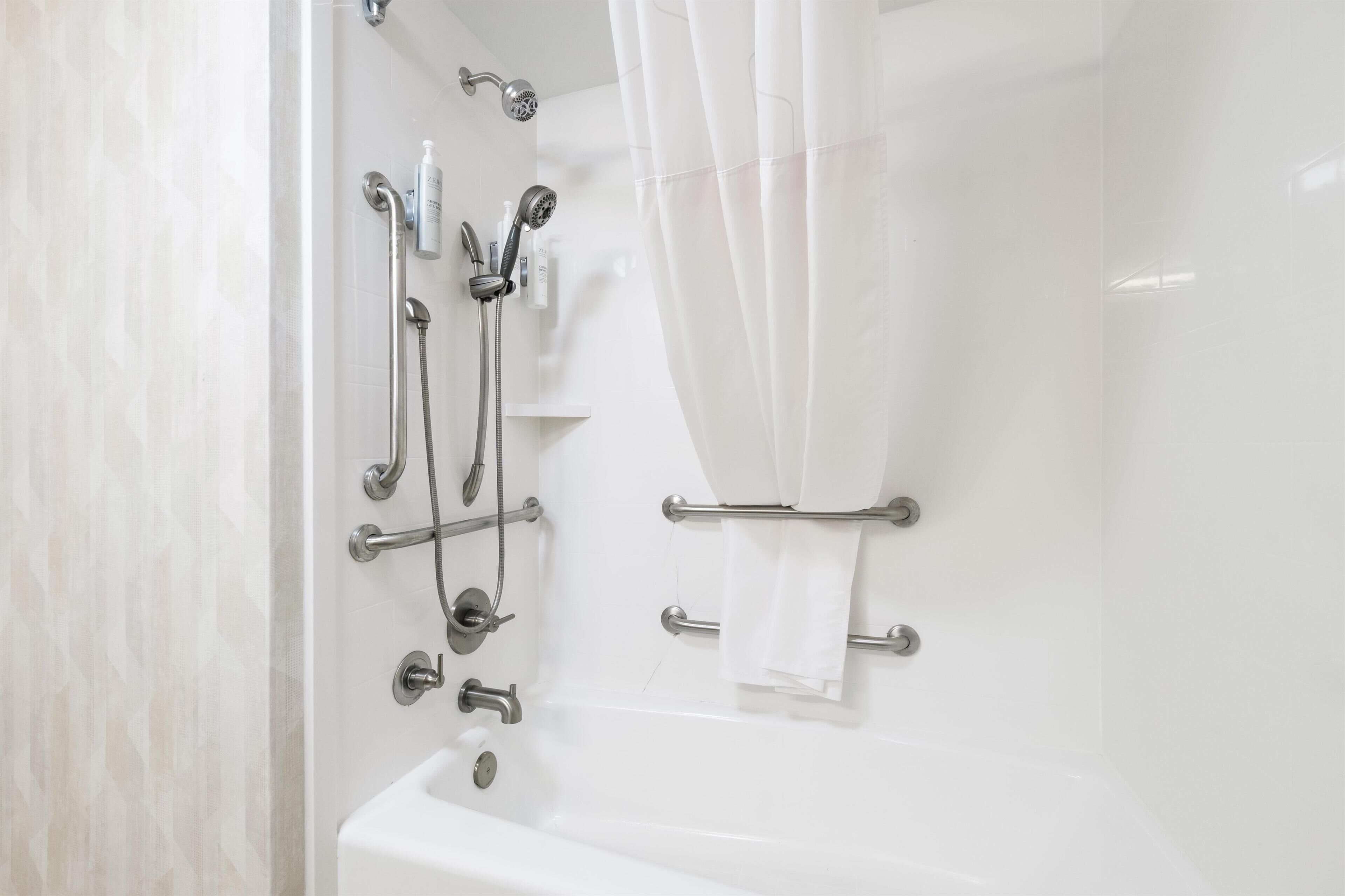A modern bathroom with a bathtub, shower, and handrails.