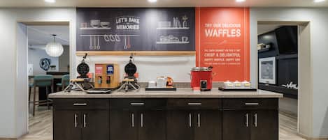 A kitchen area with a central island, a chalkboard with baking instructions, and a red sign promoting waffles.
