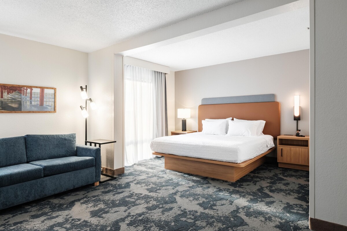 Een hotelkamer met een bed, een slaapbank, een nachtkastje, een lamp en een schilderij aan de muur.