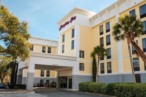 Een hotel met een heldere ingang, een bord waarop 'Hampton Inn' staat en een parkeerplaats.