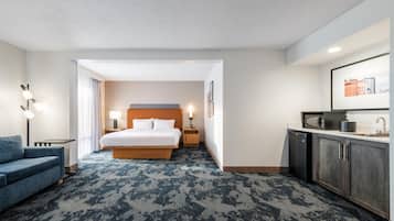 A hotel room with a bed, a desk, a chair, a microwave, a sink, and a large window.