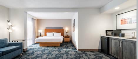A hotel room with a bed, a desk, a chair, a microwave, a sink, and a large window.