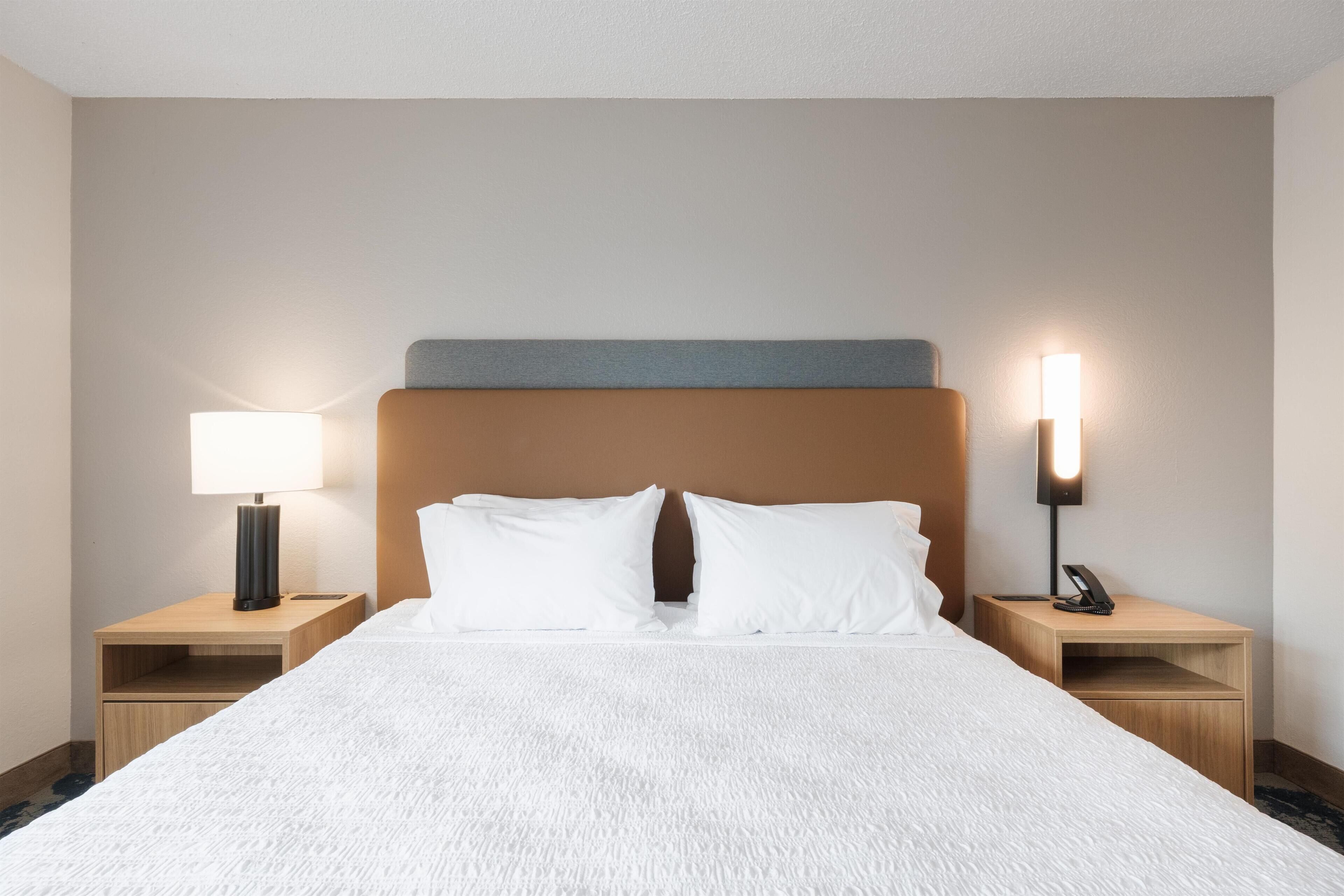 Ett hotellrum med en stor säng, två sängbord, ett litet bord, en lampa och en telefon på det lilla bordet.