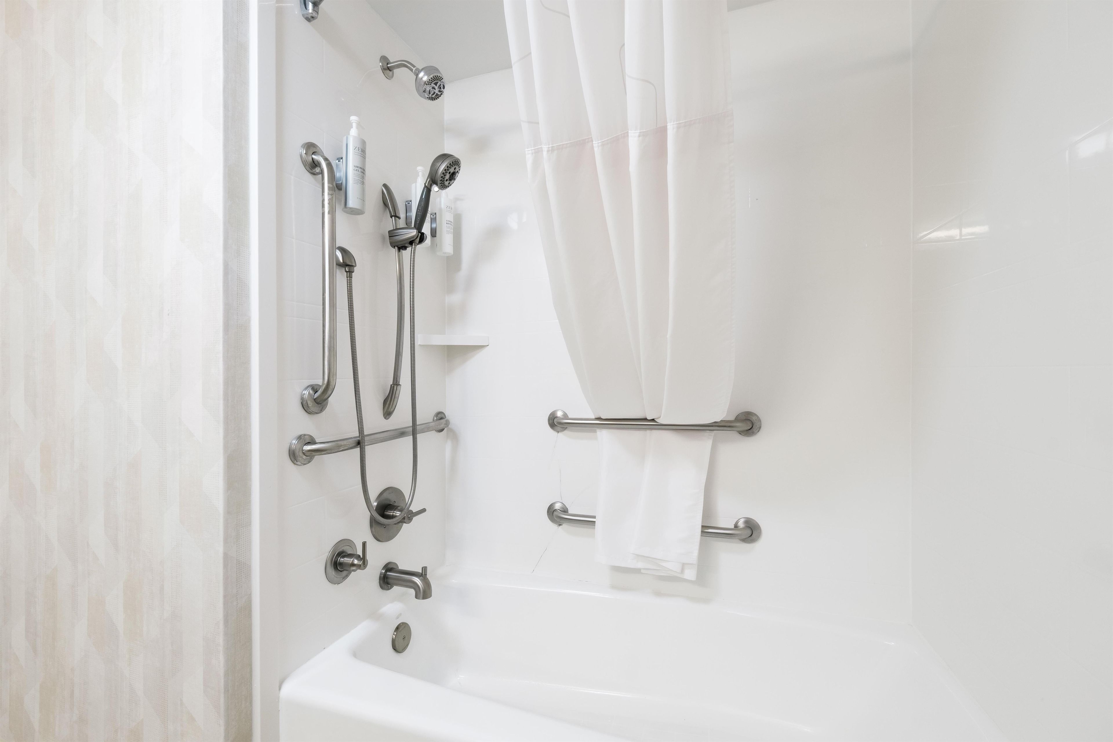 A modern bathroom with a bathtub, shower, and handrails.