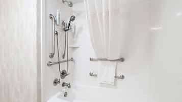 A modern bathroom with a bathtub, shower, and handrails.