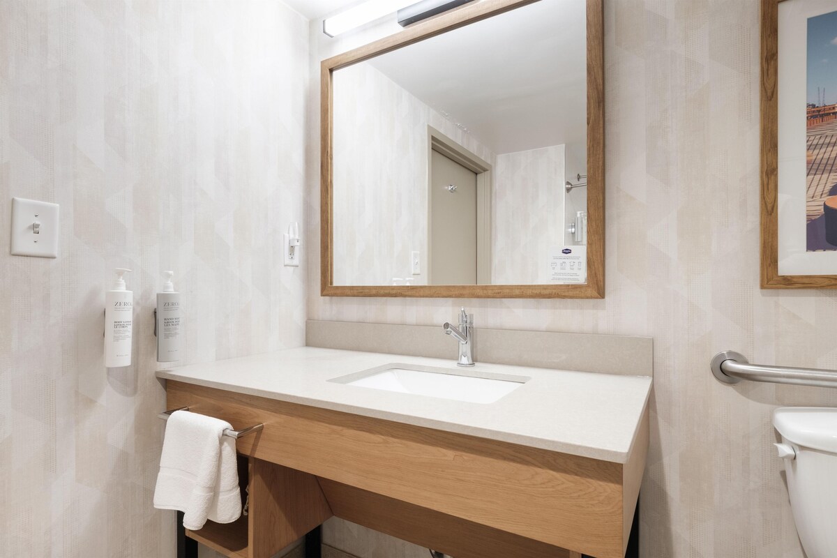 Een badkamer met een houten wastafelmeubel, een witte wastafel, een spiegel en een handgreep.