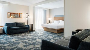 Una habitación de hotel con cama, sofá, escritorio, lámpara y un cuadro en la pared.