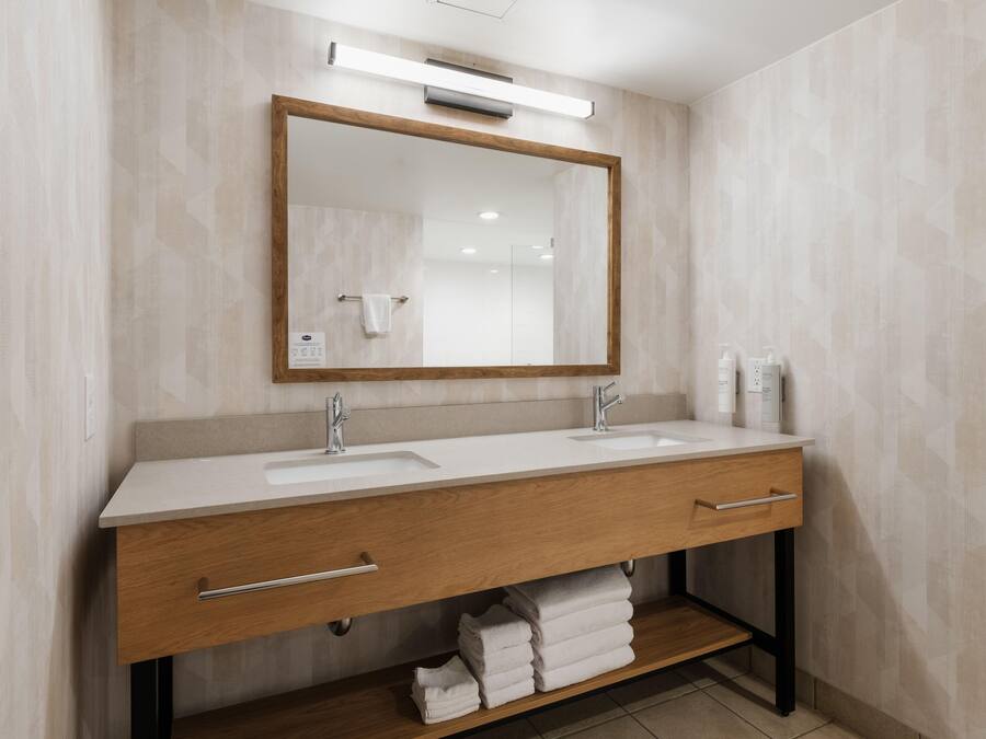 Une salle de bain moderne avec un meuble-lavabo en bois, deux vasques, un grand miroir et une étagère à serviettes.