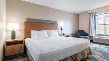 A hotel room with a large bed, a bedside table with a lamp, a chair, and a window with curtains.
