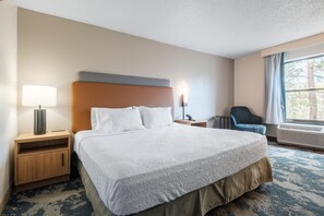 A hotel room with a large bed, a bedside table with a lamp, a chair, and a window with curtains. - Hampton Inn North Myrtle Beach-Harbourgate (North Myrtle Beach)
