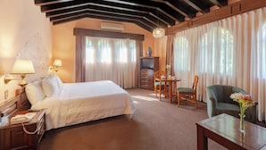 Una habitación de hotel con una cama grande, un escritorio con lámpara, una silla, un sofá y un florero con flores.