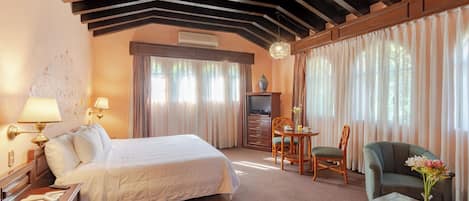 Une chambre d’hôtel avec un grand lit, un bureau avec une lampe, une chaise, un canapé et un vase de fleurs.