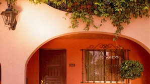 Un edificio con puerta de madera, una ventana con rejas decorativas y una planta en maceta en el suelo.