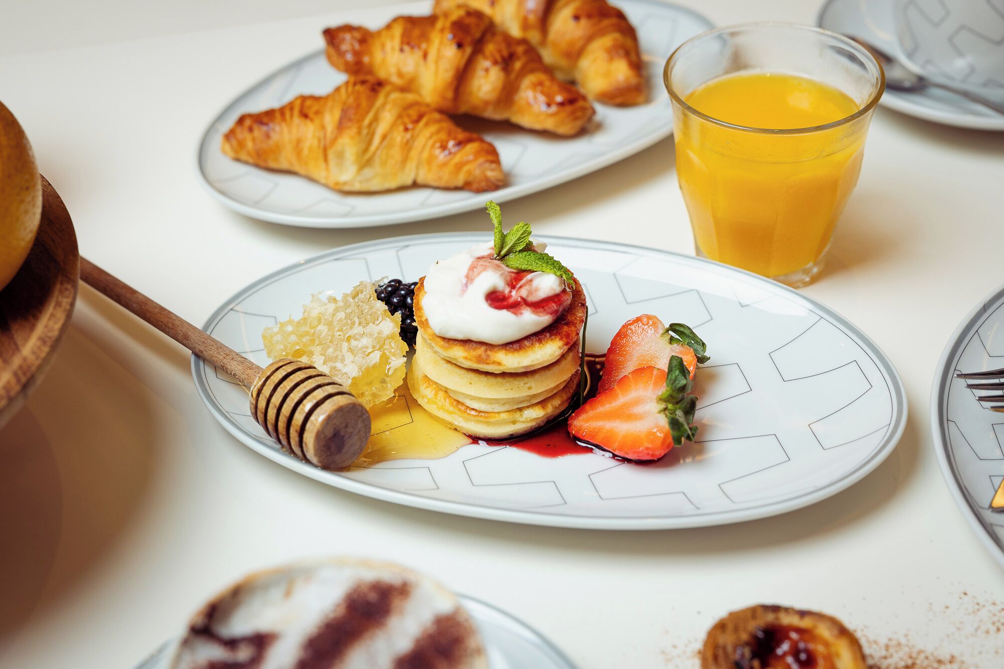 A breakfast plate with pancakes, strawberries, honey, and a croissant.