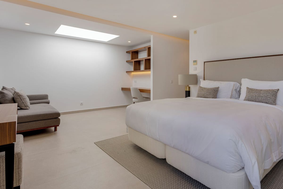 A modern bedroom with a large bed, a sofa, a desk, and a built-in shelving unit.