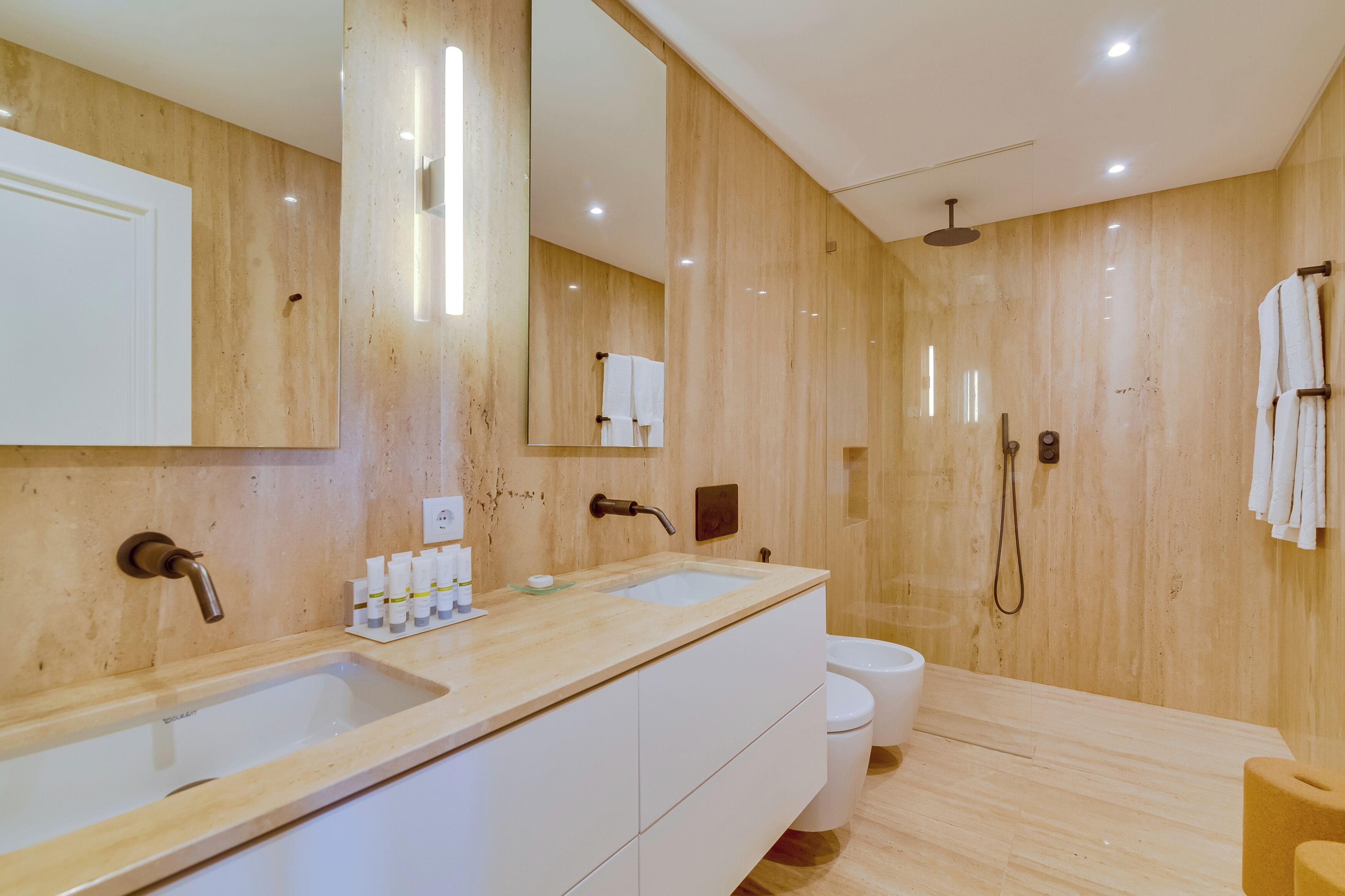 A modern bathroom with two sinks, a large mirror, a shower, and a toilet.