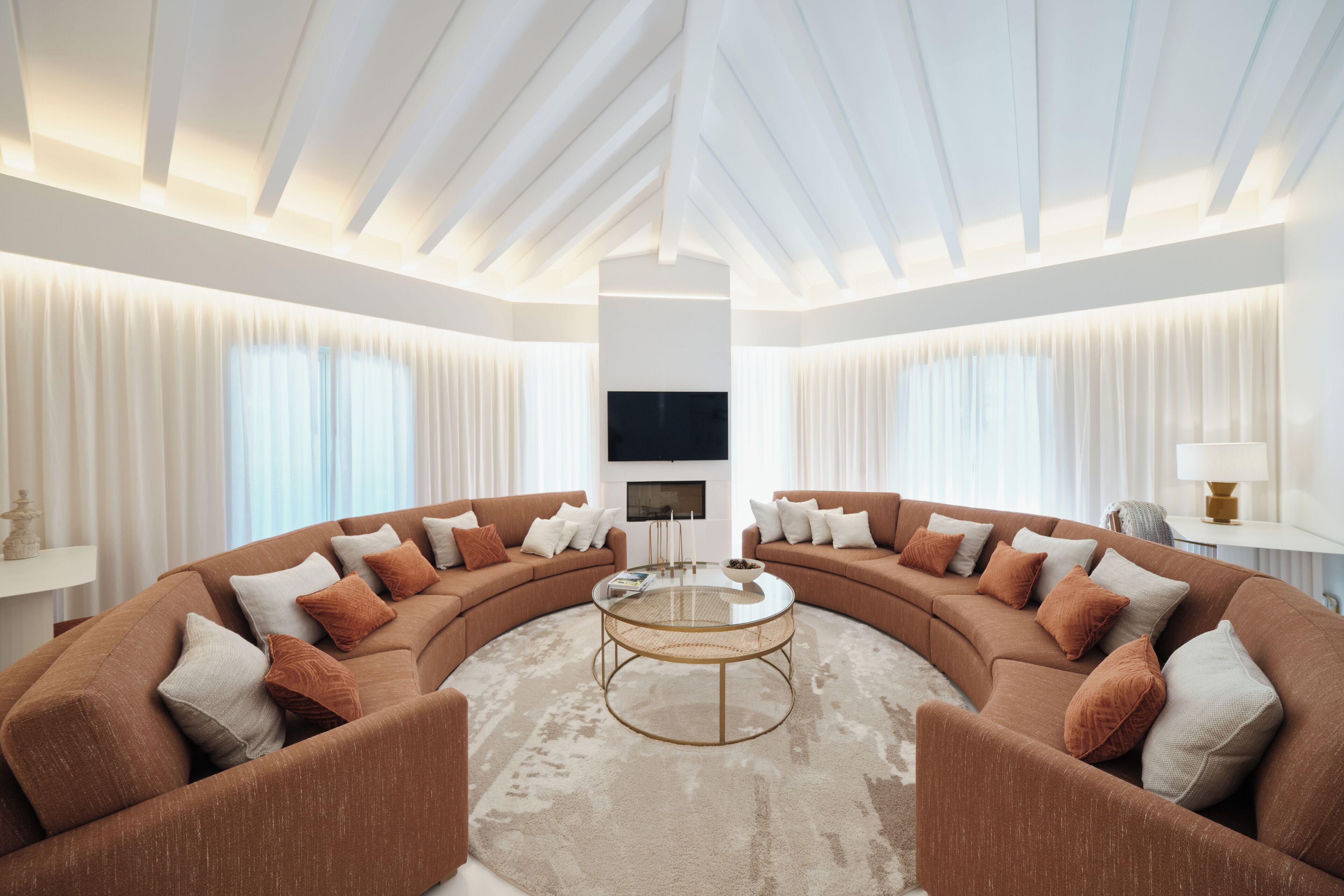 A modern living room with a curved sectional sofa, a round coffee table, and a flat-screen TV mounted on the wall.